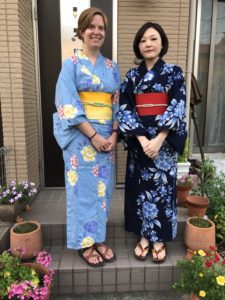 The woman on the left wears a light blue yukata with a yellow obi. On the right is a woman dressed in a dark blue yukata with a red obi.