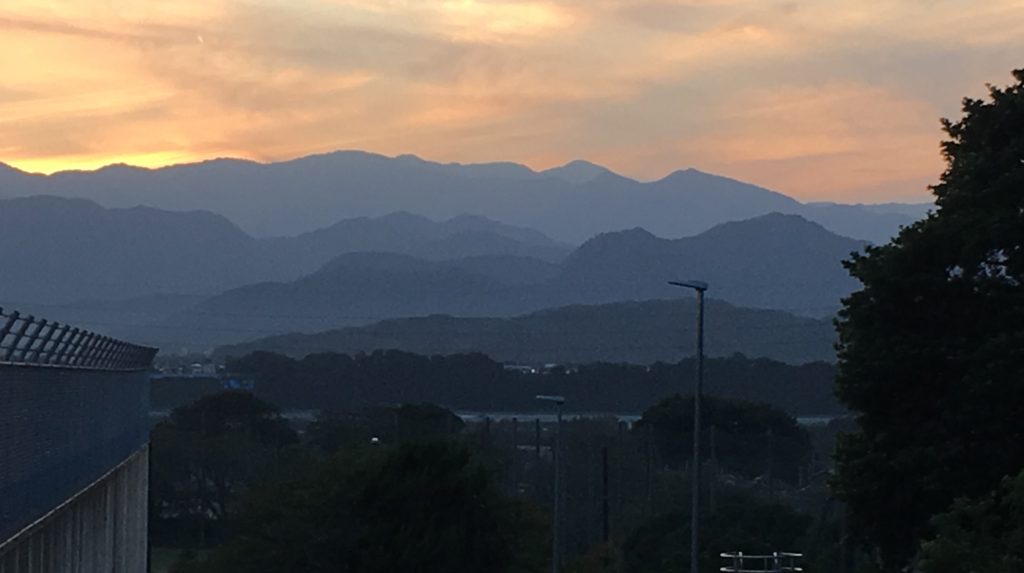 A yellow and orange sun sets behind four rows of mountains