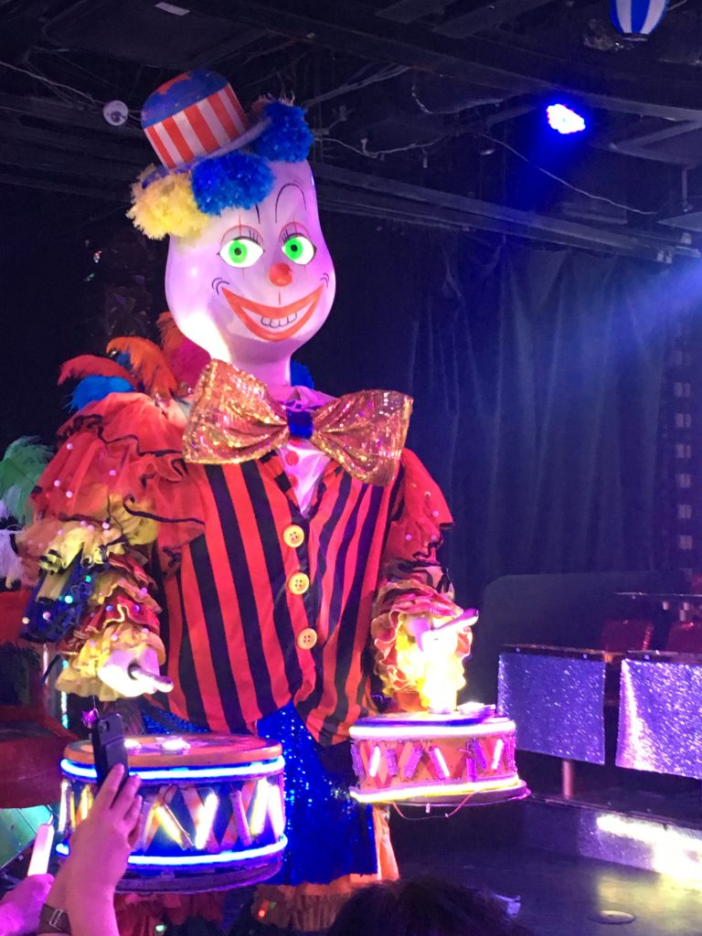 A large animatronic clown playing drums