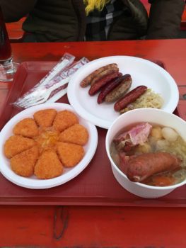 A wheel of fried cheese, a plate of sausage and a bowl of soup