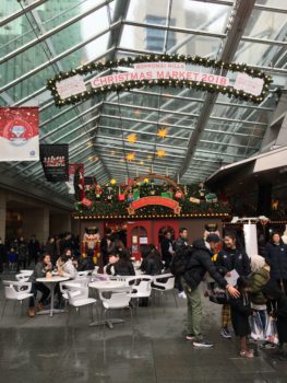 A banner marks the entrance to the market. There are stalls and some white tables and chairs
