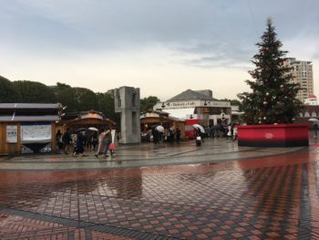 Three small wooden huts with a Christmas tree on the right.