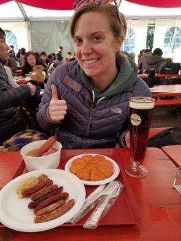 A woman in a coat sits at a red picnic table in front of German food