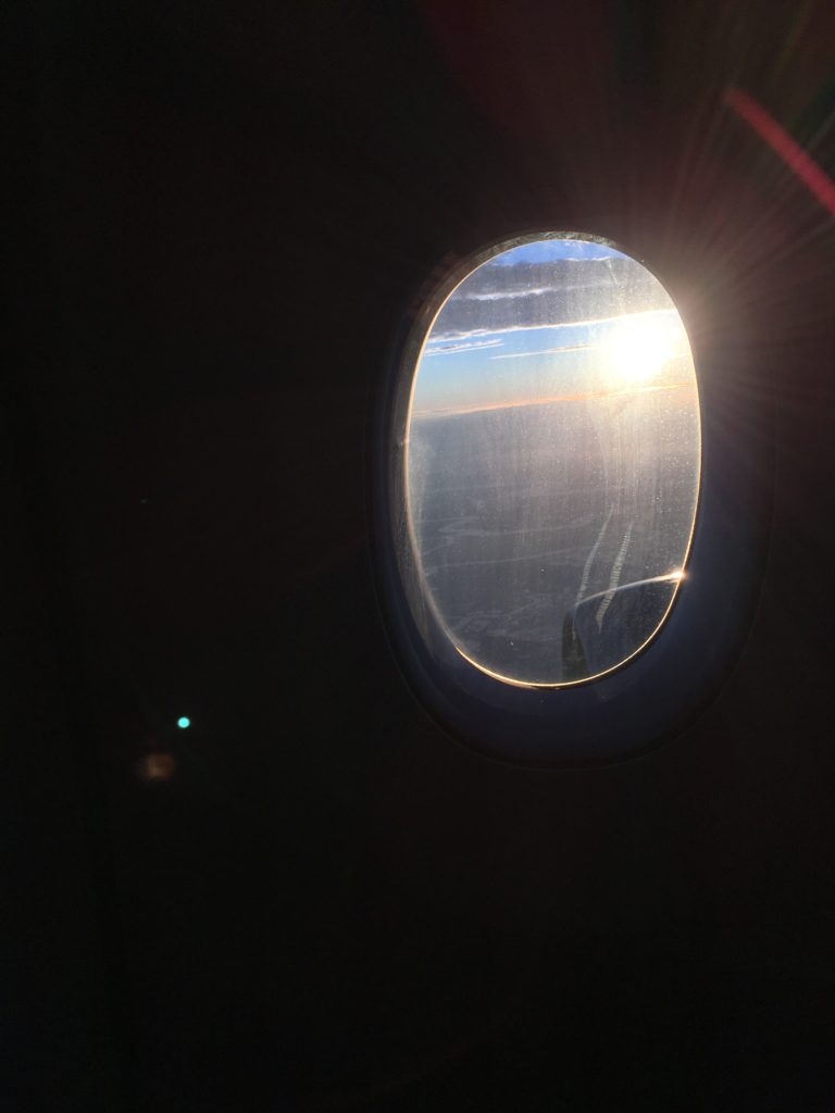 A dark foreground with an airplane window, through which you can see the setting sun