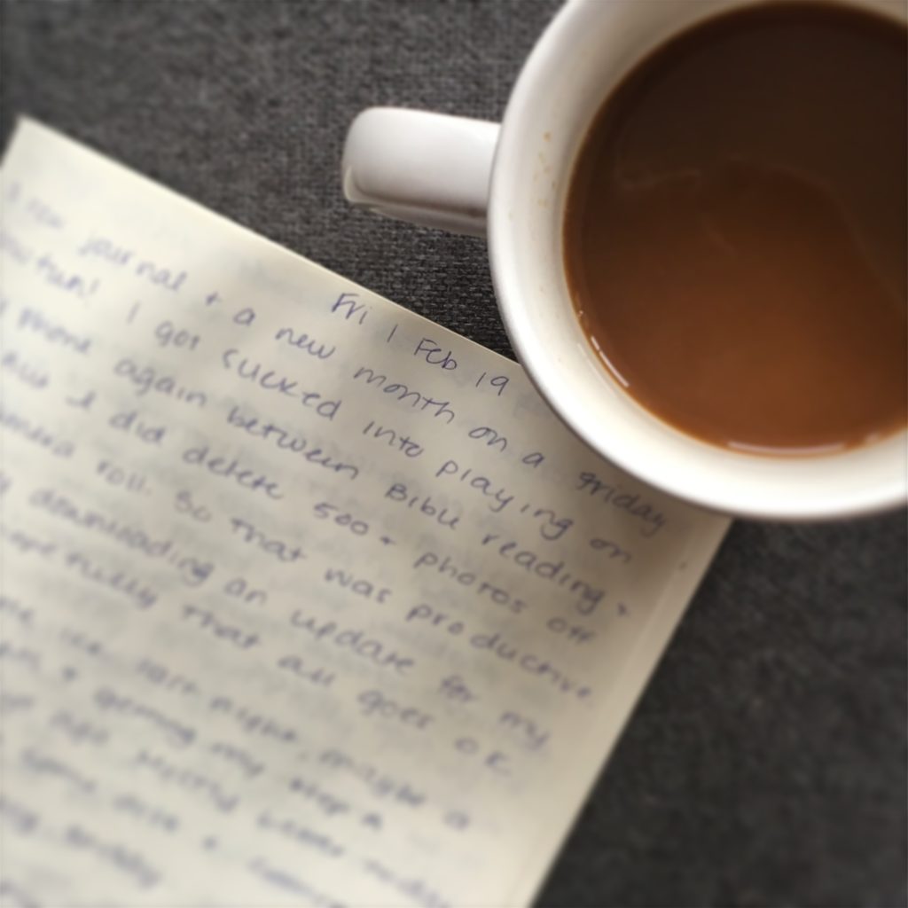 A cup of coffee is in the upper right of the photo. To the left are blurred out journal pages