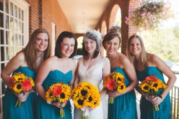 Four women in teal bridesmaids dresses surround a bride in her gown