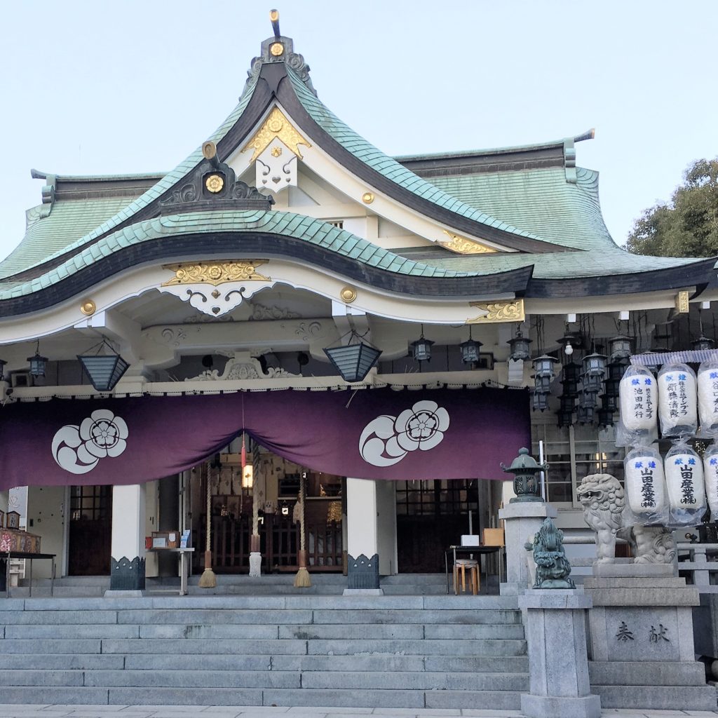 Shrine building decorated for the new year. Paper lanterns flank the sides of the building, which is green, white and gold.