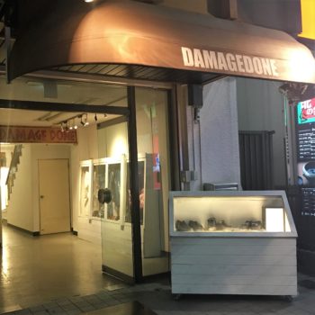 An exterior awning and small case sit outside the entrance to thrift store Damage Done